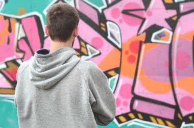 Gri kapüşonlu bir genç grafiti sanatçısı bir duvara yağmurlu havalarda pembe ve yeşil renklerde onun graffiti ile duvara görünüyor. Sokak sanatı kavramı