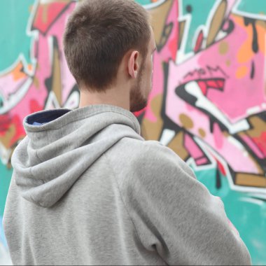 Gri kapüşonlu bir genç grafiti sanatçısı bir duvara yağmurlu havalarda pembe ve yeşil renklerde onun graffiti ile duvara görünüyor. Sokak sanatı kavramı