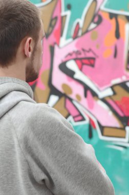 Gri kapüşonlu bir genç grafiti sanatçısı bir duvara yağmurlu havalarda pembe ve yeşil renklerde onun graffiti ile duvara görünüyor. Sokak sanatı kavramı