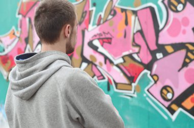 Gri kapüşonlu bir genç grafiti sanatçısı bir duvara yağmurlu havalarda pembe ve yeşil renklerde onun graffiti ile duvara görünüyor. Sokak sanatı kavramı