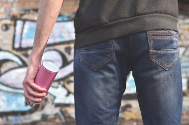 Mavi kirli kot ve gri kazak genç bir adamın eski bir tuğla duvar grafiti çizim boyalı arka planı elinde kullanılan boya sprey ile vücudun arka görünüm