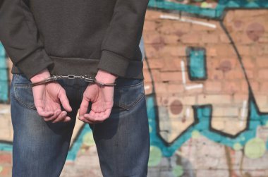 Dikiz graffiti arka planı tutuklandı ve kelepçeli suçlu. Özel mülke zarar verme, vandalizm önlenmesi ve holiganizmi mücadele kavramı. Kabalıkla kavramı