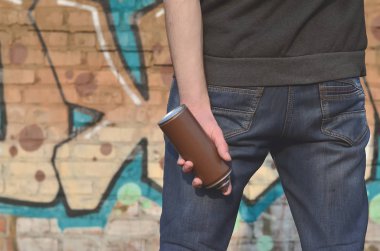 Mavi kirli kot ve gri kazak genç bir adamın eski bir tuğla duvar grafiti çizim boyalı arka planı elinde kullanılan boya sprey ile vücudun arka görünüm