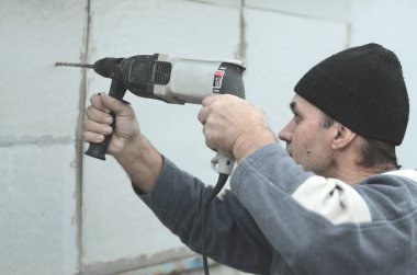 Yaşlı bir işçi bir plastik dübel takviye izleyen yüklemesi için styrofoam duvarında bir delik matkap. Delik duvara bir matkapla oluşturmak. Bina cephe Isınma