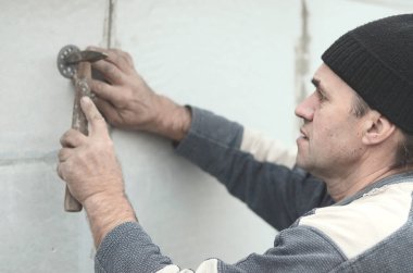 Yaşlı bir işçi Strafor duvarındaki bir plastik şemsiye bağlama içine bir dübel takunya. Genişletilmiş polistiren levhalar sabitleme işlemi. Bina cephe ısınma