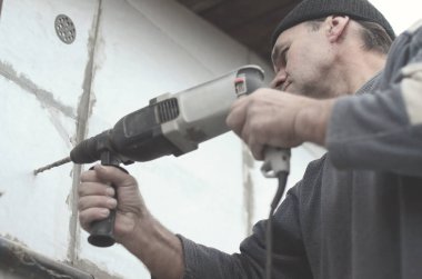Yaşlı bir işçi bir plastik dübel takviye izleyen yüklemesi için styrofoam duvarında bir delik matkap. Delik duvara bir matkapla oluşturmak. Bina cephe Isınma