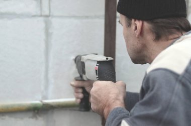 Yaşlı bir işçi bir plastik dübel takviye izleyen yüklemesi için styrofoam duvarında bir delik matkap. Delik duvara bir matkapla oluşturmak. Bina cephe Isınma