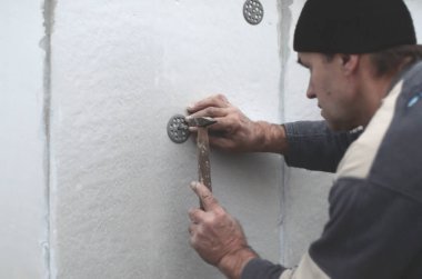 Yaşlı bir işçi Strafor duvarındaki bir plastik şemsiye bağlama içine bir dübel takunya. Genişletilmiş polistiren levhalar sabitleme işlemi. Bina cephe ısınma