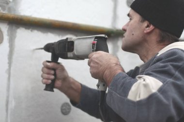Yaşlı bir işçi bir plastik dübel takviye izleyen yüklemesi için styrofoam duvarında bir delik matkap. Delik duvara bir matkapla oluşturmak. Bina cephe Isınma