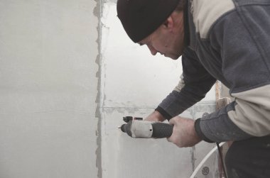Yaşlı bir işçi bir plastik dübel takviye izleyen yüklemesi için styrofoam duvarında bir delik matkap. Delik duvara bir matkapla oluşturmak. Bina cephe Isınma