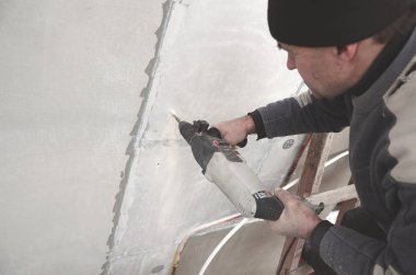 Yaşlı bir işçi bir plastik dübel takviye izleyen yüklemesi için styrofoam duvarında bir delik matkap. Delik duvara bir matkapla oluşturmak. Bina cephe Isınma