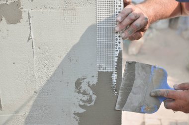 Ev yenilenen araçları sıvama duvar ile eski bir işçi elleri. Sıvacı yenilenen açık duvar ve spatula ve alçı ile köşeleri. Duvar izolasyonu. İnşaat bitirme işleri