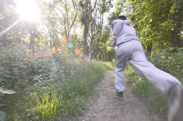 A young guy in a gray sports suit runs along the path among the trees in the forest. Sports jogging outdoors. Movement effect