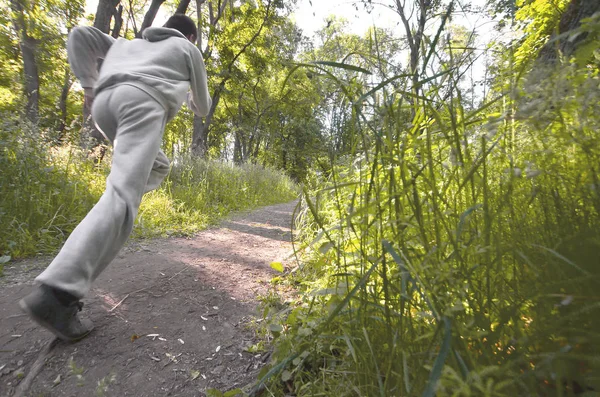 A young guy in a gray sports suit runs along the path among the trees in the forest. Sports jogging outdoors. Movement effect