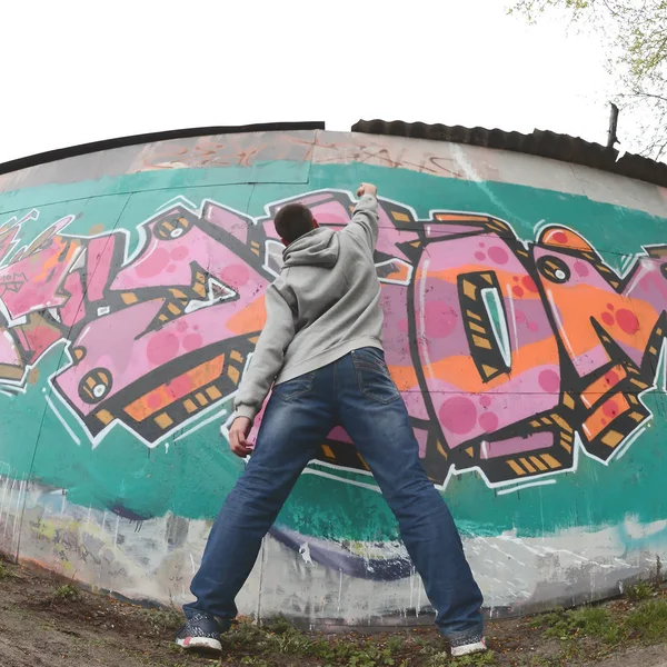 Mladý Muž Šedém Hoodie Maluje Graffiti Růžové Zelené Barvy Zeď — Stock fotografie