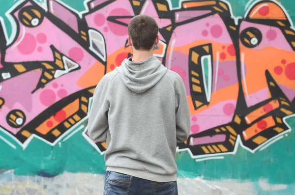 Gri kapüşonlu bir genç grafiti sanatçısı bir duvara yağmurlu havalarda pembe ve yeşil renklerde onun graffiti ile duvara görünüyor. Sokak sanatı kavramı