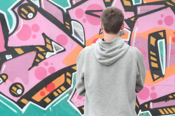 Gri kapüşonlu bir genç grafiti sanatçısı bir duvara yağmurlu havalarda pembe ve yeşil renklerde onun graffiti ile duvara görünüyor. Sokak sanatı kavramı