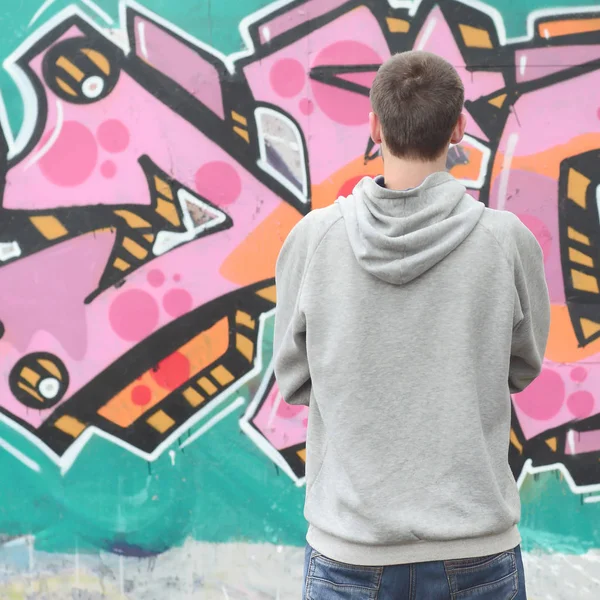 Gri kapüşonlu bir genç grafiti sanatçısı bir duvara yağmurlu havalarda pembe ve yeşil renklerde onun graffiti ile duvara görünüyor. Sokak sanatı kavramı