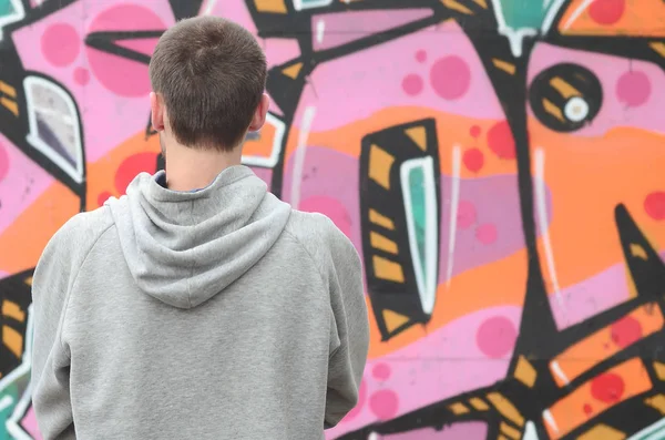 Gri kapüşonlu bir genç grafiti sanatçısı bir duvara yağmurlu havalarda pembe ve yeşil renklerde onun graffiti ile duvara görünüyor. Sokak sanatı kavramı