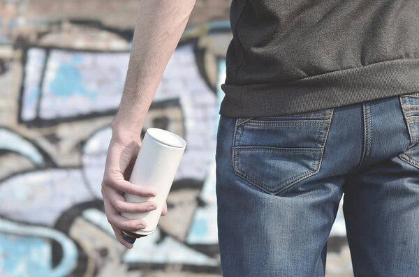 Фото хулигана, который портит государственную собственность, красит стены аэрозольной краской. Фрагмент тела молодого преступника с распылителем краски в грязной руке. Проблема повреждения имущества
