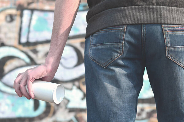A photo of a bully who spoils state property, paints walls with aerosol paint. Fragment of the body of a young criminal vandal with a paint sprayer in a dirty hand. Problem of damage to property