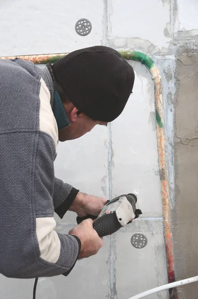 Yaşlı bir işçi bir plastik dübel takviye izleyen yüklemesi için styrofoam duvarında bir delik matkap. Delik duvara bir matkapla oluşturmak. Bina cephe Isınma
