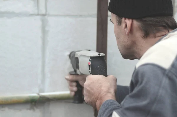 An elderly workman drills a hole in a styrofoam wall for the subsequent installation of a plastic reinforcing dowel. Creating holes in the wall with a drill. Warming of the building facade — Stock Image Elderly Workman Drills Hole Styrofoam Wall Subsequent Installation Plastic Reinforcing Stock Picture