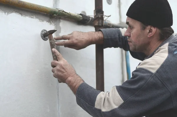 An elderly workman clogs a dowel into a plastic umbrella mount in a styrofoam wall. The process of fixing expanded polystyrene plates. Warming of the facade of the building — Stock Image Elderly Workman Clogs Dowel Plastic Umbrella Mount Styrofoam Wall Process Stock Image