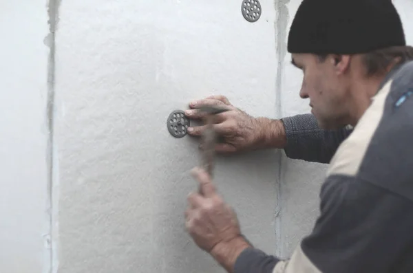 An elderly workman clogs a dowel into a plastic umbrella mount in a styrofoam wall. The process of fixing expanded polystyrene plates. Warming of the facade of the building — Stock Image Elderly Workman Clogs Dowel Plastic Umbrella Mount Styrofoam Wall Process Stock Photo