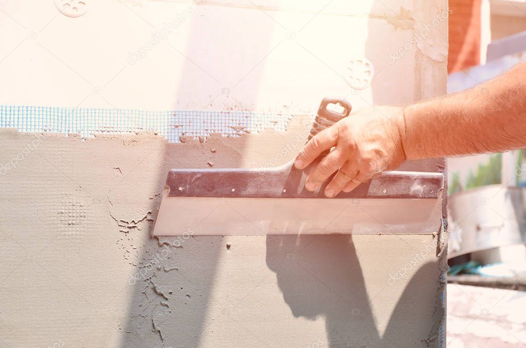 Hands of an old manual worker with wall plastering tools renovating house. Plasterer renovating outdoor walls and corners with spatula and plaster. Wall insulation. Construction finishing works