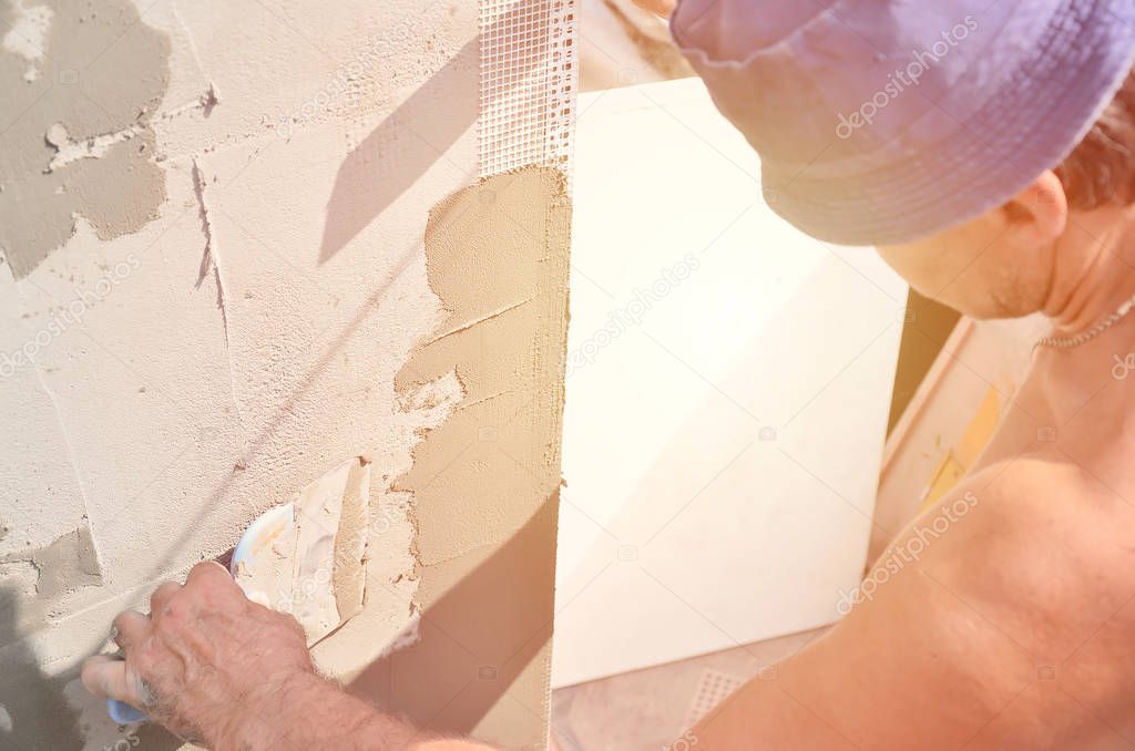 Fifty years old manual worker with wall plastering tools renovating house. Plasterer renovating walls and corners with spatula and plaster. Wall mash installation. Construction finishing works