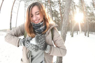 Kahverengi bir ceket genç ve neşeli beyaz kız kış aylarında karla kaplı bir ormandaki bir kartopu sculpts. Açık havada kar oyunlar. Balıkgözü fotoğraf