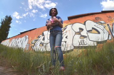 Siyah saçlı ve piercing ile duygusal bir genç kız portresi. Sprey boya... kutularını graffiti duvar arka plan üzerinde elinde bir kızla bir geniş açı fotoğraf. Bir balıkgözü lens modern bir portresi