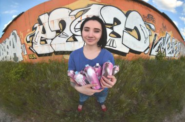 Siyah saçlı ve piercing ile duygusal bir genç kız portresi. Sprey boya... kutularını graffiti duvar arka plan üzerinde elinde bir kızla bir geniş açı fotoğraf. Bir balıkgözü lens modern bir portresi