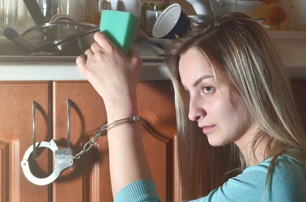 スポンジ 悲しい 疲れた女の子の肖像画は多くの洗っていない皿 プレート カップ カトラリー 台所のカウンターに手錠をかけられ キッチンで作業する女性を強制の概念 — ストック写真