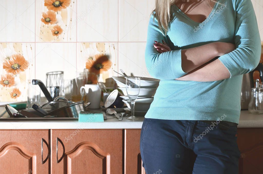 Fragment of the female body at the kitchen counter, filled with a lot of unwashed dishes. The girl is tired of coping with the daily duty of washing dishes. Problems of family life