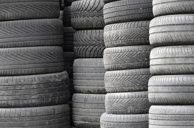 Old used tires stacked with high piles in secondary car parts shop garage close up clipart
