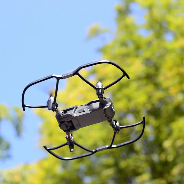 Drone with photocamera take off from land and flying for take aerial photo at sunset evening front of trees