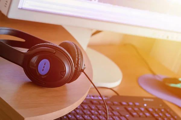 Big black headphones lie on the wooden desktop of the sound designer. Workplace for music creator. Selective focus