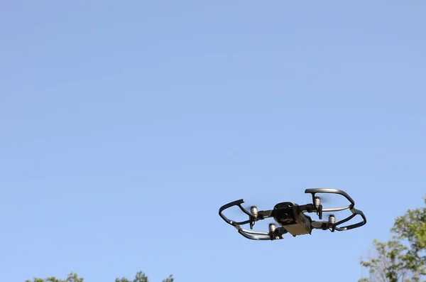 Drone with photocamera take off from land and flying for take aerial photo at sunset evening front of trees