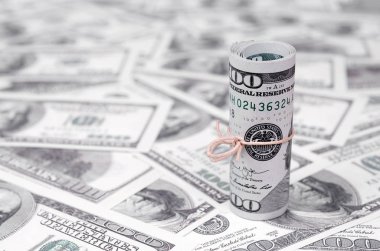 Bize dolar haddelenmiş ve grup ile sıkılaştırılmış bir sürü Amerikan banknotları bulanık arka plan ile yatıyor. Para büyük miktarda