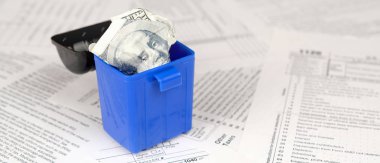 Birçok Amerikan vergisi boş formları ve çöp kutusunda yüz dolarlık banknotu. Vergiler kavramı ödemek için para kaybı