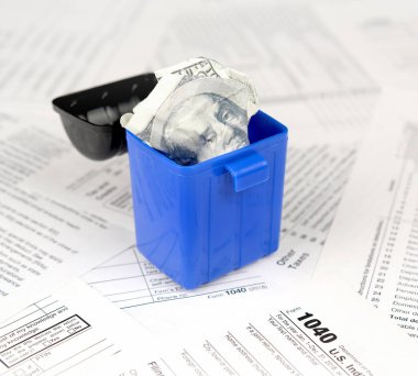 Birçok Amerikan vergisi boş formları ve çöp kutusunda yüz dolarlık banknotu. Vergiler kavramı ödemek için para kaybı