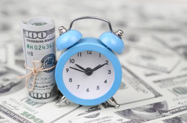 Zaman yönetimi konsepti. Mavi çalar saat yüz dolarlık faturaları büyük miktarda yatıyor. İş içinde önemli kaynaklardan biri olarak zaman