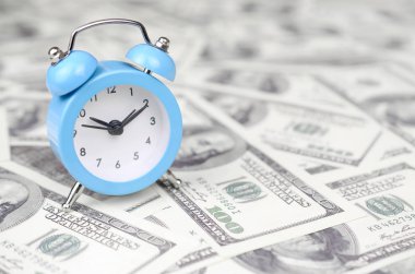 Zaman yönetimi konsepti. Mavi çalar saat yüz dolarlık faturaları büyük miktarda yatıyor. İş içinde önemli kaynaklardan biri olarak zaman