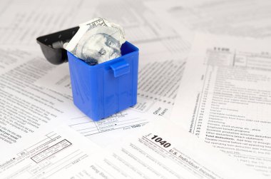 Birçok Amerikan vergisi boş formları ve çöp kutusunda yüz dolarlık banknotu. Vergiler kavramı ödemek için para kaybı