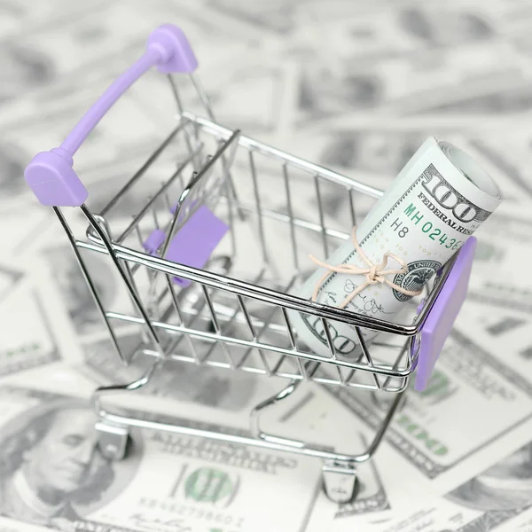 Small shopping trolley with dollars banknotes. Big amount of US dollar bills and shopping cart. Concept of cashback and bargains on sale