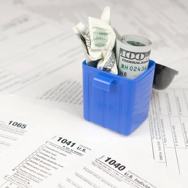 Birçok Amerikan vergisi boş formları ve çöp kutusunda yüz dolarlık banknotu. Vergiler kavramı ödemek için para kaybı