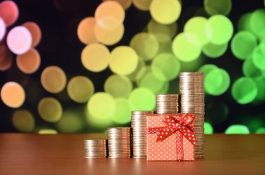 Renkli bokeh arka planda küçük kırmızı hediye kutusu ve altın sikke yığınları