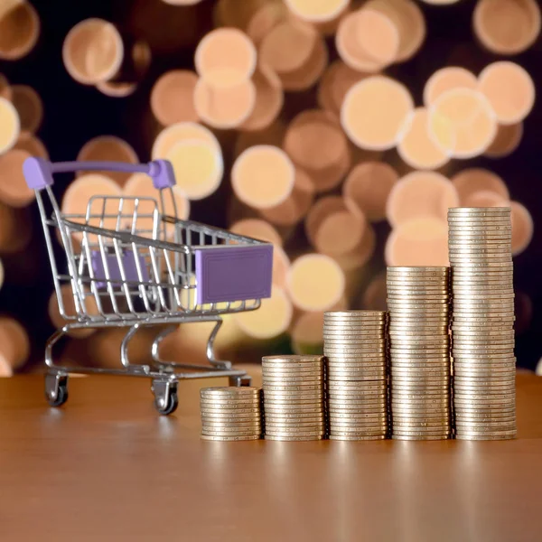 Empty shopping cart and money stacks in growth graph on background of colored bokeh christmas lights — Stock Photo, Image